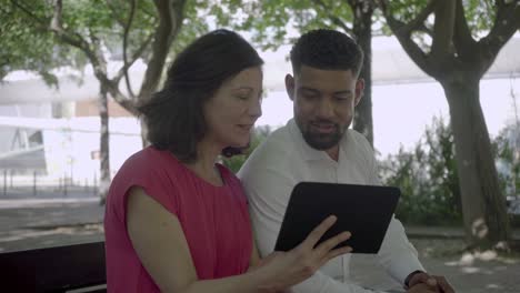 Happy-multiracial-couple-using-tablet-in-park.
